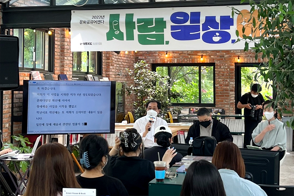 부산문화재단 ‘2022년 문화공유어젠다-사람, 일상, 예술’ 내 ‘2022 부산 장애예술인 활동 실태조사 중간발표회’. 행사명 현수막이 걸려있는 벽돌로 지은 공간에 사람들이 가득하다. 