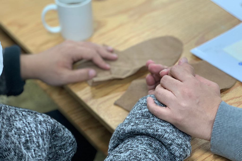 라움콘 두 작가가 서로의 한 손을 맞잡고 있다. 테이블에는 손 모양의 본 한 쌍이 놓여 있다. 