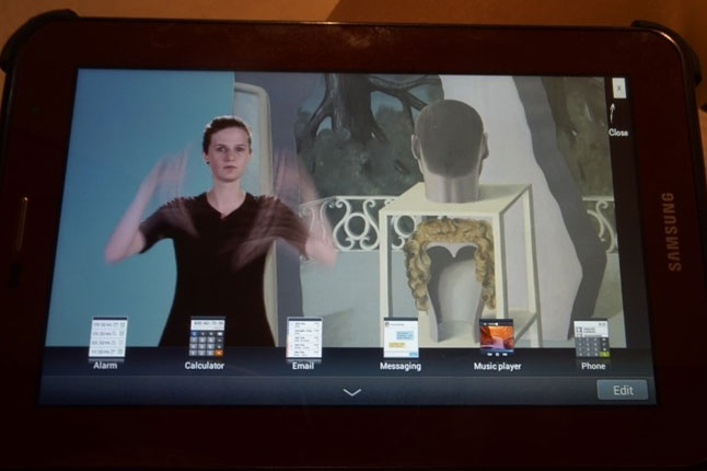 벨기에왕립미술관의 수어해설 비디오 가이드 패드. 작품을 배경으로 왼편에 수어해설사 모습이 나타나있다. 하단에는 선택할 수 있는 다른 메뉴가 떠 있다.