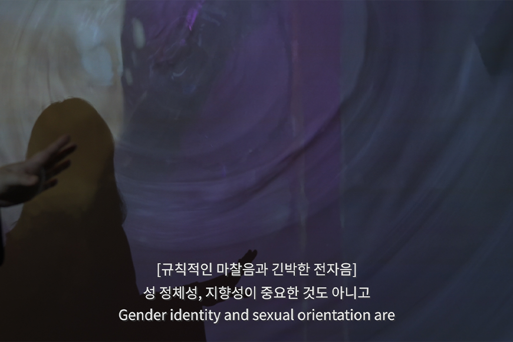 질퍽한 질감의 배경에 보랏빛 조명이 비추고, 한 사람의 그림자와 그가 앞으로 뻗은 손이 보인다. 폐쇄자막은 [규칙적인 마찰음과 긴박한 전자음]. 자막은 성 정체성, 지향성이 중요한 것도 아니고 Gender identity and sexual orientation are.