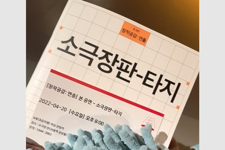 격자 무늬 바탕에 창작공감:연출 <소극장판-타지>가 쓰인 팸플릿, 해당 공연의 티켓이 그 위에 겹쳐 있다.