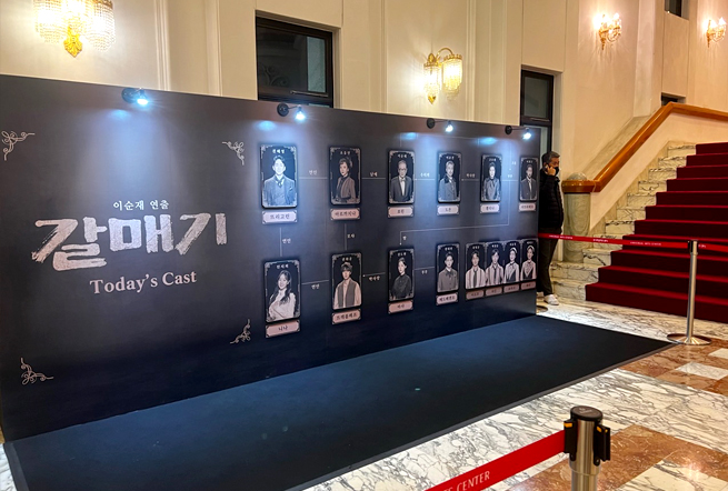 연극 갈매기의 공연장 포토존. 왼편에 크게 타이틀이 써 있고, 오른편에 오늘의 캐스트 14명 배우들의 사진이 역할별로 붙어 있다.