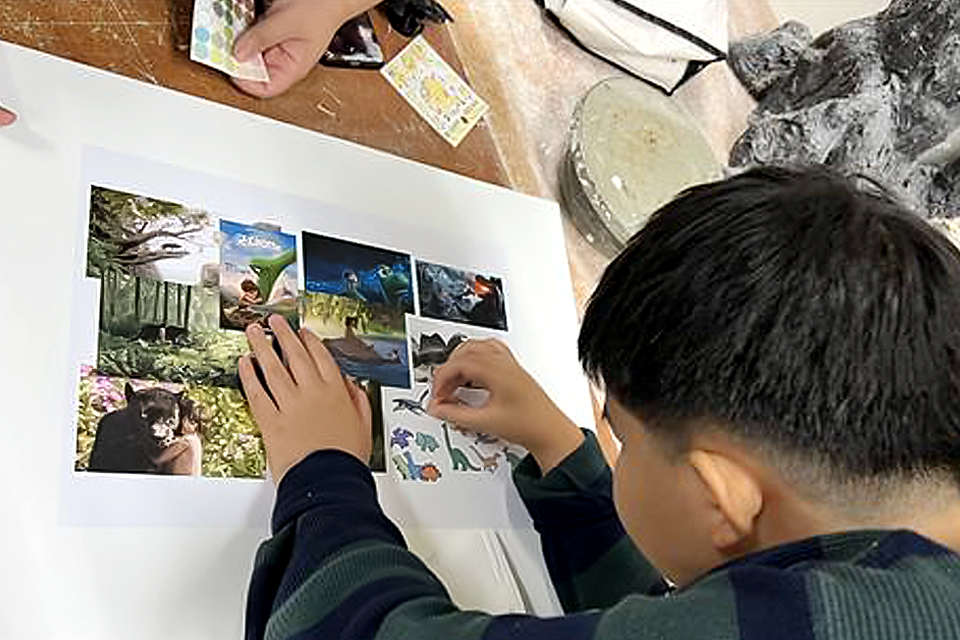 지성이가 책상 위에 놓인 콘셉트 보드에서 마음에 드는 사진에 스티커를 붙이고 있다.