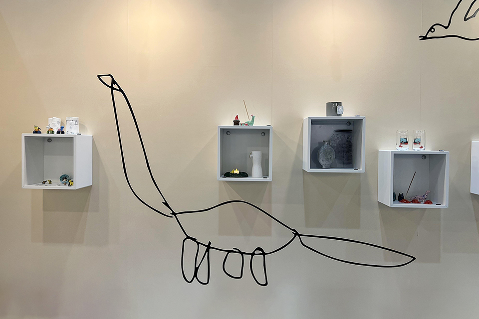 전시벽에 사각박스 5개가 나란히 붙어 있고 박스 안과 위에 작은 도예 소품이 놓여 있다. 빈 벽면에는 지성이의 커다란 공룡 그림이 있다.