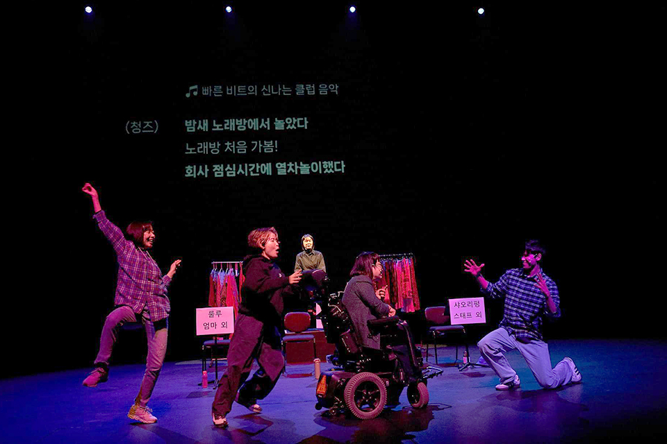 네 배우가 각각 신나는 몸짓을 한다. 그들 뒤로 수어통역사가 보인다. 자막에는 “밤새 노래방에서 놀았다. 노래방 처음 가봄! 회사 점심시간에 열차놀이했다”라고 쓰여있다.