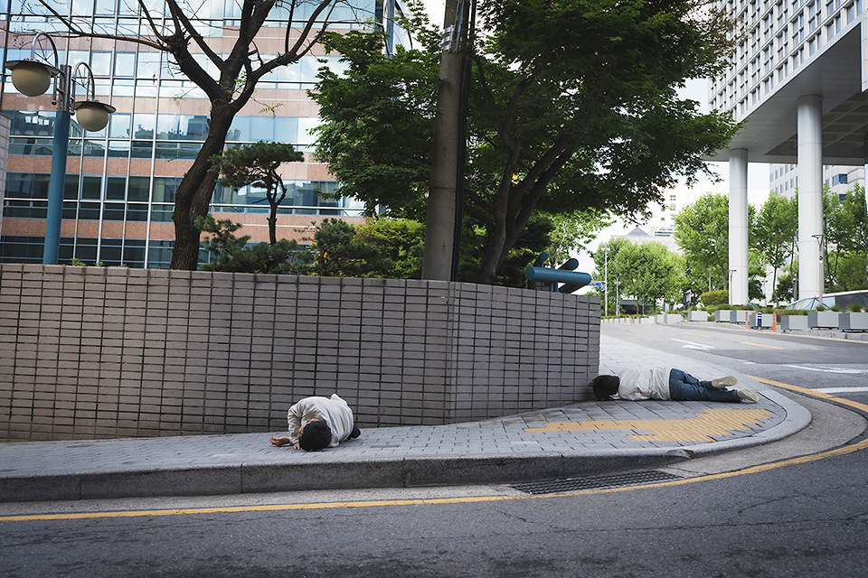 한적한 도로 옆 보행로에서 퍼포머 두 사람이 구르고 있다. 