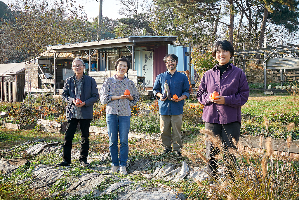 네 사람이 농장 건물 계단에 걸터 앉아 환하게 미소짓고 있다.