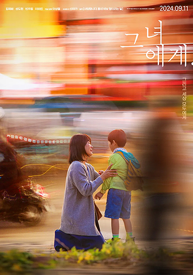 엄마가 무릎을 꿇고 앞에 서 있는 아이의 두 팔을 붙들고 있다. 배경에는 도시의 불빛이 화려하게 섞여 흐른다. 오른쪽 상단에 ‘그녀에게’라고 쓰여 있다.
