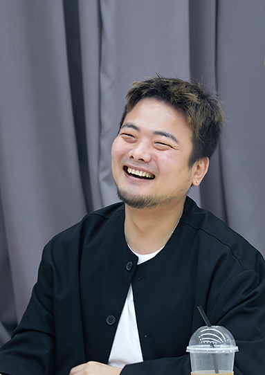 회색 커튼 앞에 우지양이 앉아서 왼쪽을 바라보며 환하게 웃고있다.