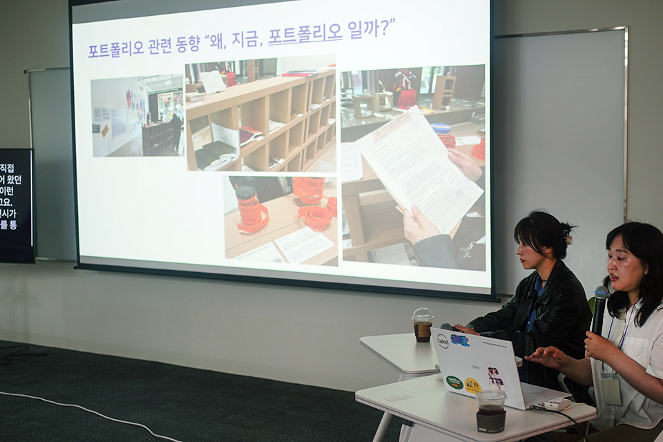 두 사람이 나란히 앉아 스크린에 영사된 자료로 강의를 하고 있다. 화면에는 ‘포트폴리오 관련 동향 “왜, 지금, 포트폴리오 일까”’라고 쓰여 있다. 옆에는 문자통역 모니터가 있다.