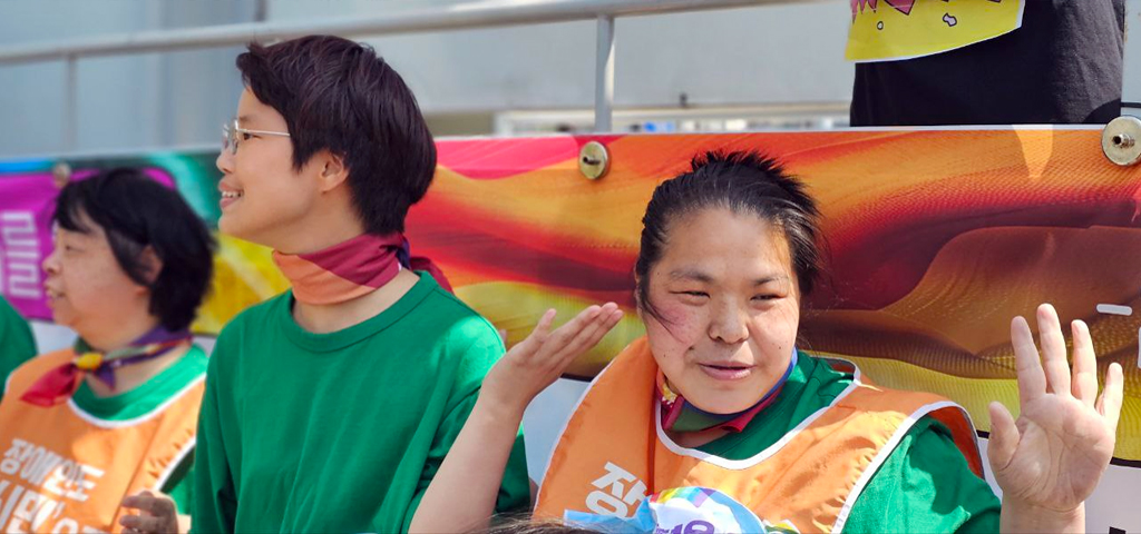 밝은 날 야외에서 초록색 옷을 입은 필자와 활동가들이 미소 지으며 한쪽 손을 들고 있다.