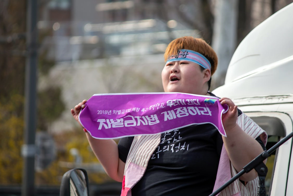 필자가 머리띠를 두르고 ‘차별금지법 제정하라’는 문구가 적힌 보라색 플랜카드를 들고 있다.