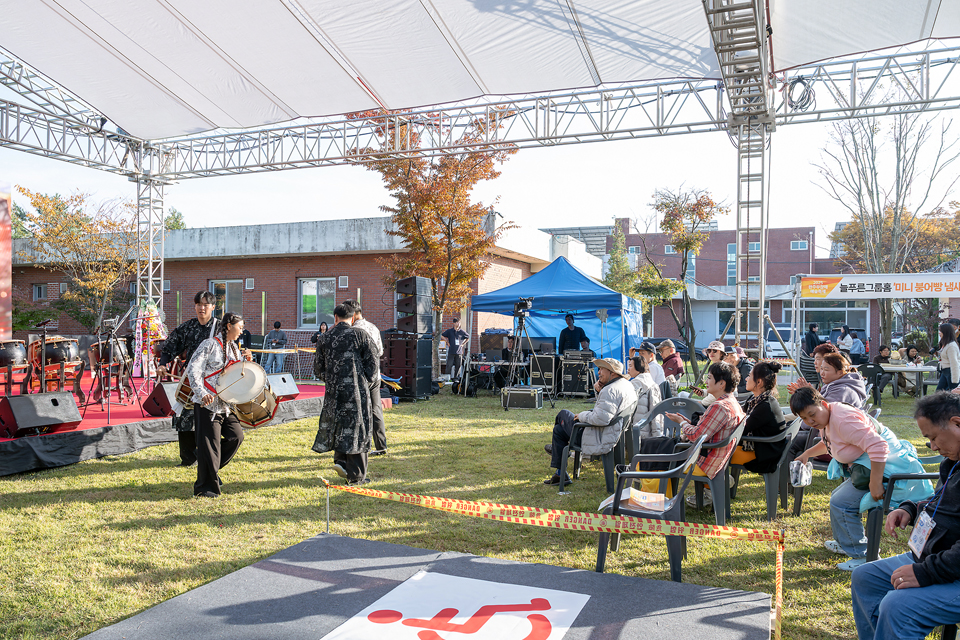 무대와 객석에 트러스를 세워 그늘을 만든 야외마당. 연주자들이 무대에서 내려와 관객석 바로 앞에서 설장구를 북을 치며 공연하고 있다. 객석 한쪽에는 휠체어석 표식이 바닥에 넓게 깔려 있다.