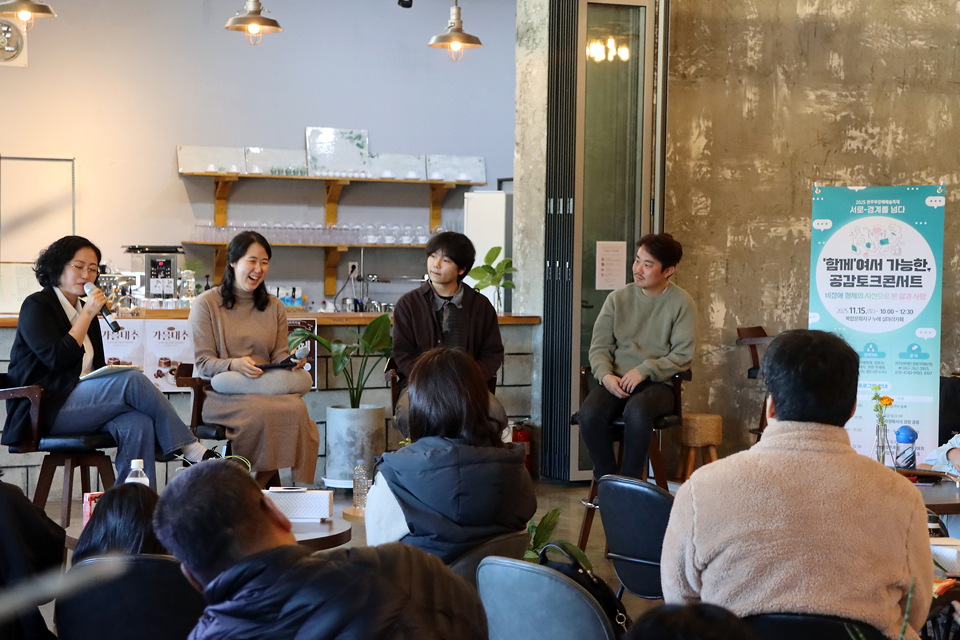 네 명의 패널이 카페형 공간에서 관객과 마주 앉아 대화를 나누고 있다. 오른쪽에 행사 배너가 세워져 있다.