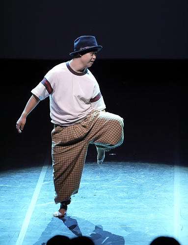 어두운 무대 위 조명 아래에서 검정색 펠트모자를 쓴 유영천이 한쪽 다리를 들고 균형을 잡은 채 춤추고 있다.