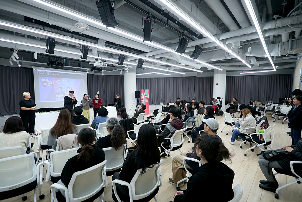 환하게 불을 밝힌 넓은 행사장에 많은 사람이 자유롭게 앉아 진행자들의 이야기에 집중하고 있다. 뒤쪽으로 영상 스크린에는 ‘이음온에어 2부 네트워킹. 나는 ○○이 소중해’라는 글과 함께 두 진행자 사진이 있다. 옆쪽에서는 수어통역사가 수어통역을 하고 있다.