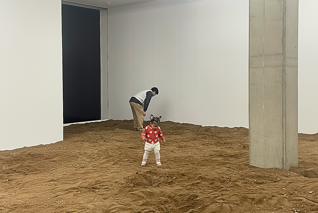 전시장 바닥을 흙으로 채운 아사드 라자의 작품 〈흡수〉 설치 전경. 어른과 어린이 관람객이 흙 위를 걸으며 공간을 체험하는 모습이 보인다.