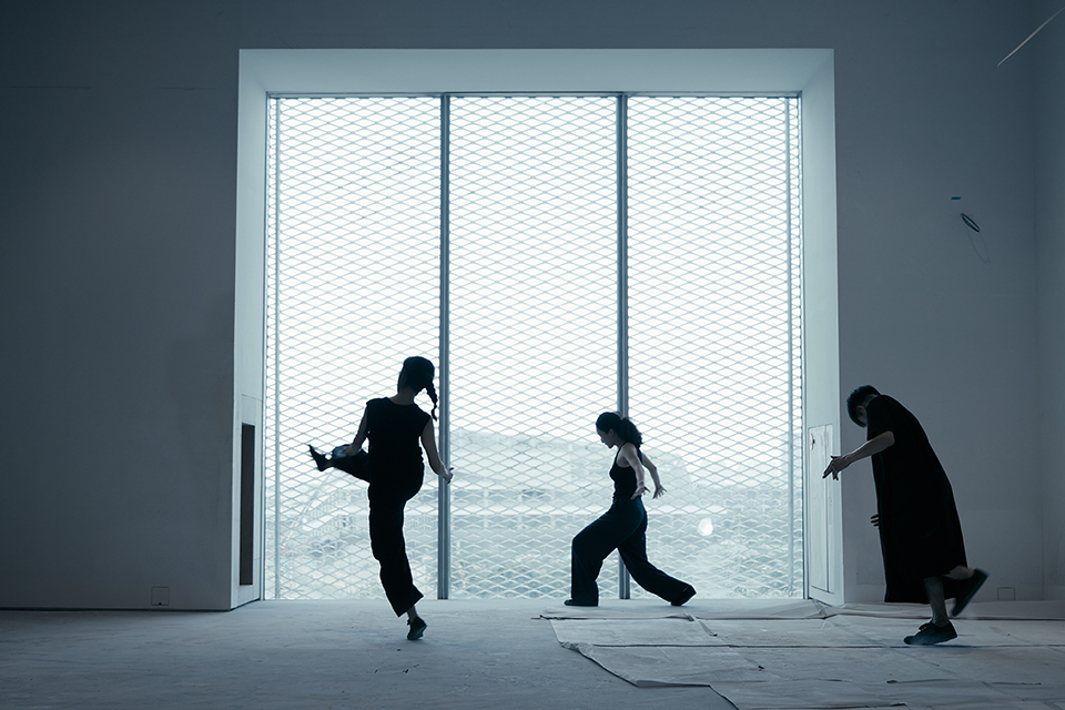 넓고 밝은 전시장 공간에서 세 명의 퍼포머가 있다. 각각 한쪽 다리를 들어 올린 채 균형을 잡고 있고,  앞으로 달리듯 몸을 기울이고, 고개를 숙인 채 천천히 이동하고 있다. 뒤쪽에는 높고 큰 투명 유리문이 설치되어 있으며, 역광으로 인해 인물들은 실루엣처럼 보인다. 