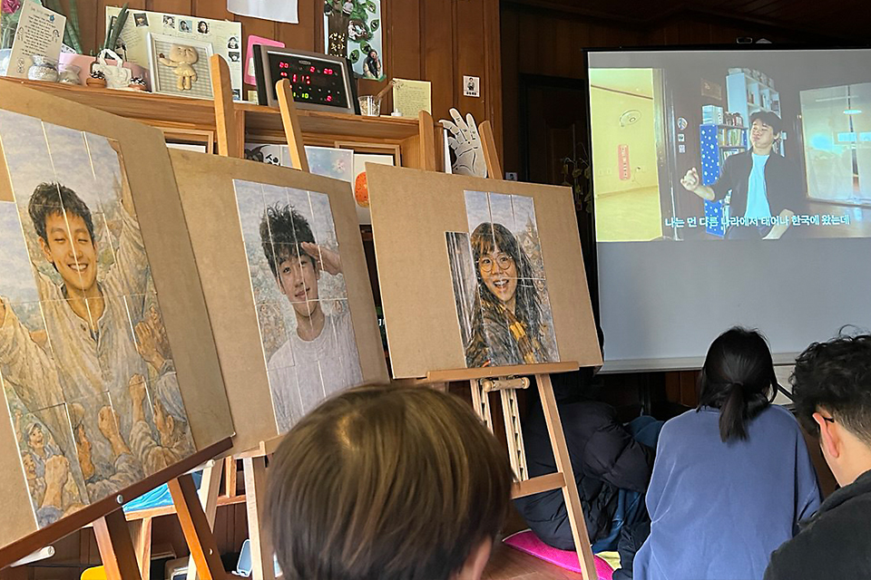 방 한쪽에 정가은, 이상일, 송요셉을 그린 퍼즐 그림카드가 놓인 세 개의 이젤이 있다. 스크린에는 ‘요셉’의 모습과 자막 영상이 나오고, 관객이 앉아서 보고 있다.