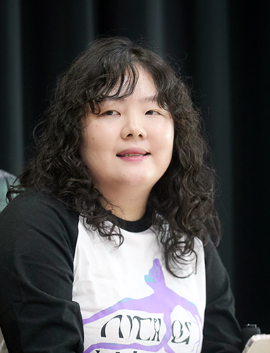 붉은 벽돌벽에 세로로 길게 난 창을 배경으로 다섯 명이 미소 지으며 카메라를 바라보고 있다. 앞의 두 사람은 휠체어에 앉아 있고, 뒤의 세 사람은 서 있다.