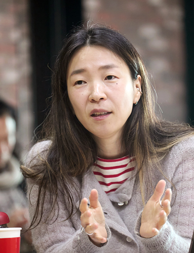 붉은 벽돌벽에 세로로 길게 난 창을 배경으로 다섯 명이 미소 지으며 카메라를 바라보고 있다. 앞의 두 사람은 휠체어에 앉아 있고, 뒤의 세 사람은 서 있다.