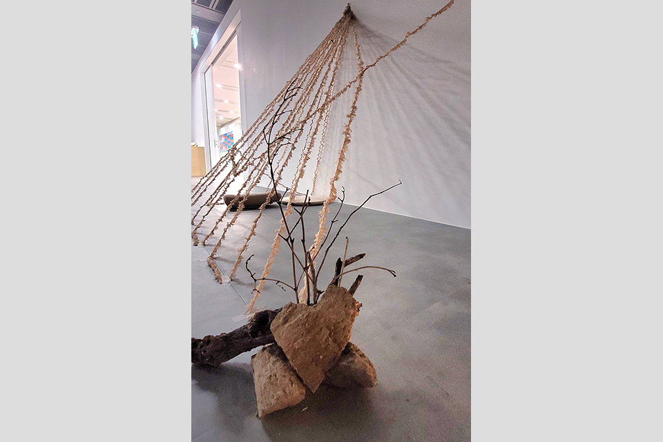 미술관 전시실의 회색 바닥과 하얀 벽을 배경으로 불규칙한 모양의 돌덩이와 마른 나뭇가지가 놓여 있다. 그 뒤로 얇은 털실이 부채꼴 모양으로 벽과 바닥을 연결하며 촘촘하게 뻗어 있다.