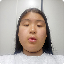 긴 머리에 회색 티셔츠를 입고 정면을 응시하는 여성. 눈은 살짝 내려다본다.