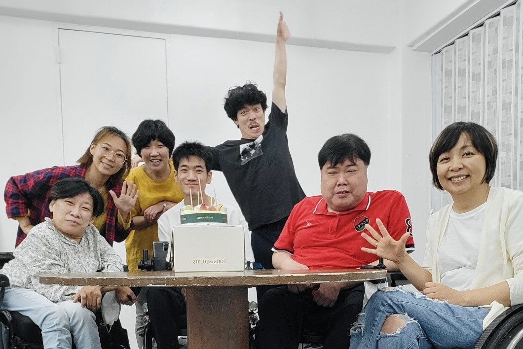 극단 애인 단원 7명의 단체사진. 원형 테이블에 모여앉아 카메라를 보며 환히 웃고있다. 테이블 위에는 케이크가 놓여있다.