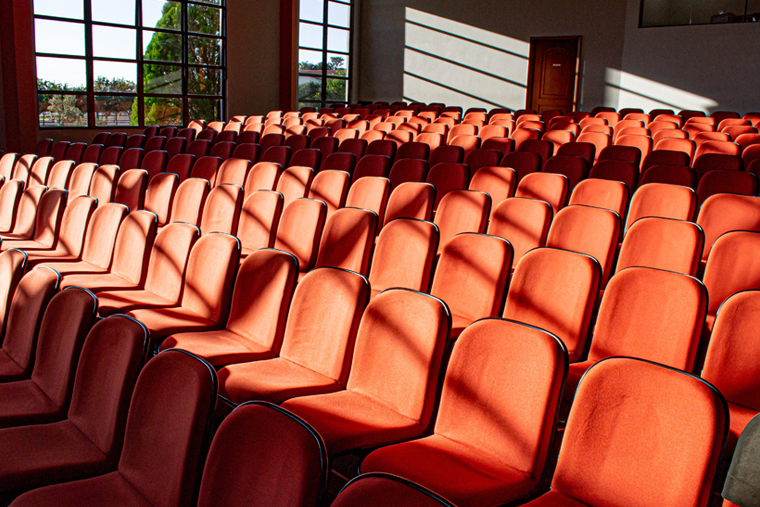의자가 가득 늘어서 있고, 창문으로 햇빛이 들어오는 극장 내부